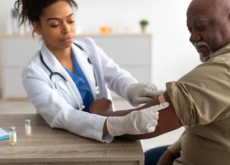 Enfermeira aplicando medicamento no braço de um paciente idoso durante atendimento domiciliar.